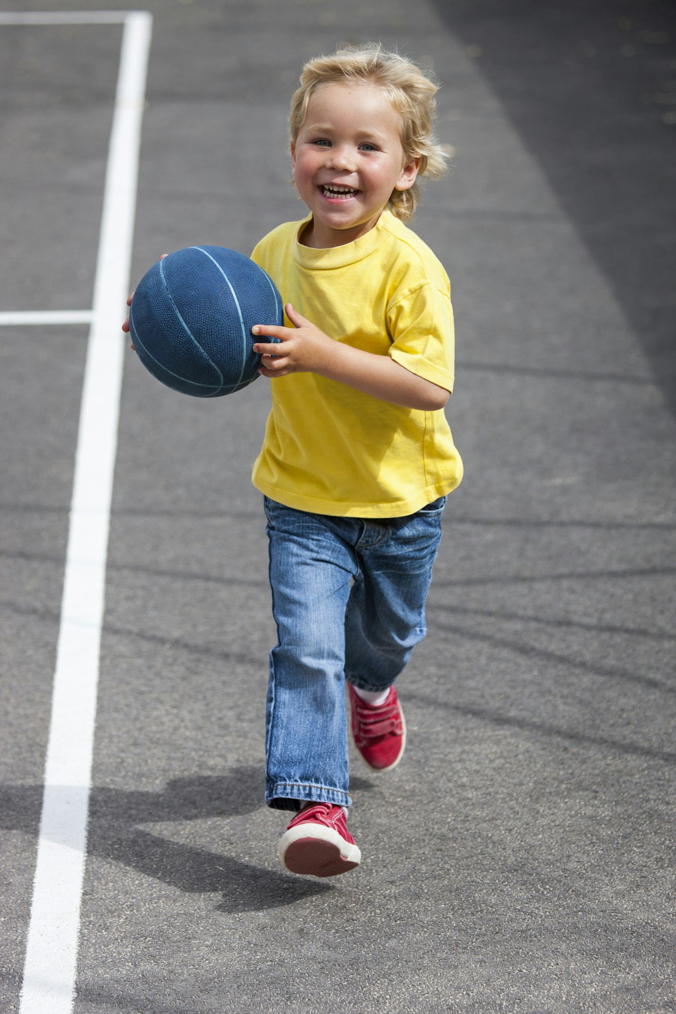 Preschool boy running with ball in preschool yard
